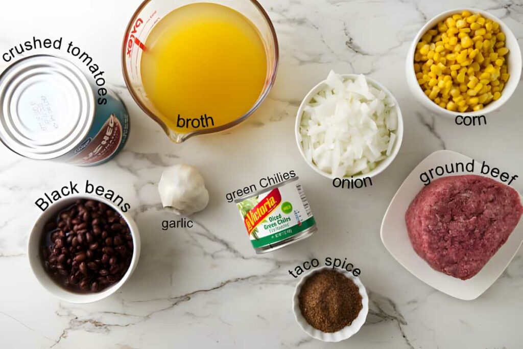 Taco soup ingredients arranged on marble: tomatoes, beef, beans, corn, spices.