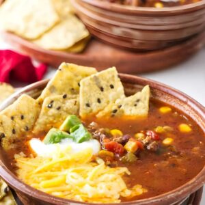 Bowl of soup with cheese, sour cream, green onions, and tortilla chips.