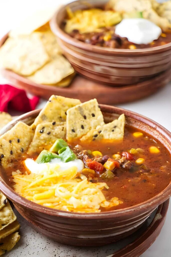 Bowl of soup with cheese, sour cream, green onions, and tortilla chips.