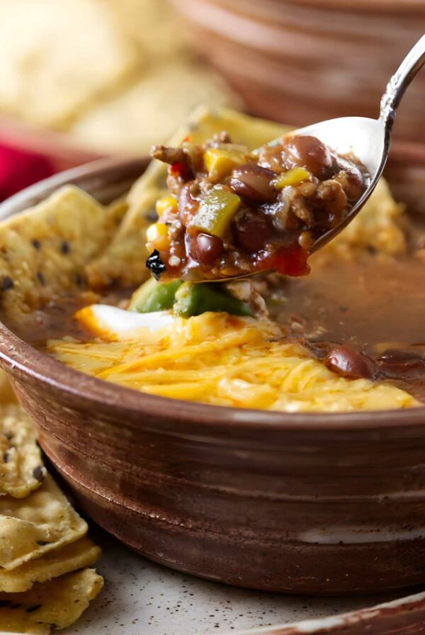 Spoonful of taco soup with beans, corn, meat; cheese-topped bowl below.