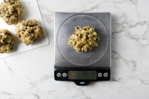 Measuring chocolate chip walnut cookie dough on a scale for 6 ounce cookies.
