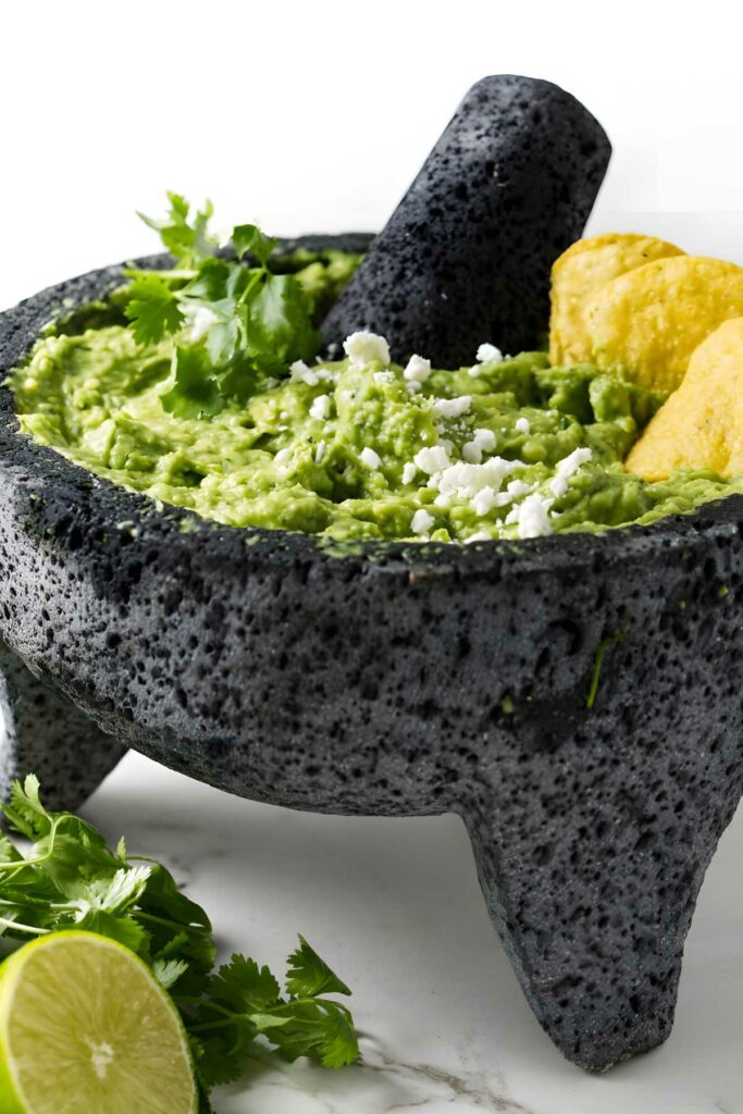 Guacamole in stone molcajete with chips, cilantro, cheese, and lime.