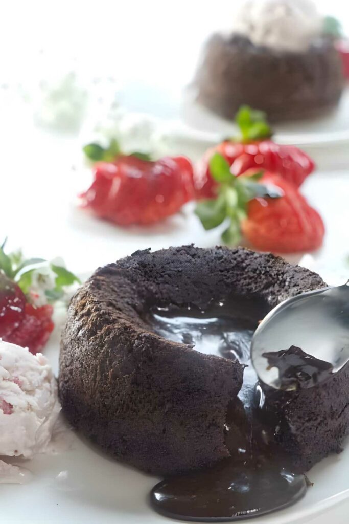 Spoon cutting chocolate lava cake with melting center, ice cream, strawberries.
