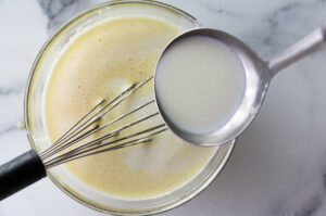 Whisking milk into a mixture in a bowl for crème mousseline.