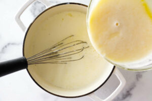 Adding tempered eggs to a pot to make custard-based buttercream.