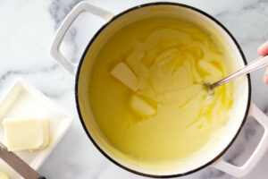 Adding butter to a pot to make creme mousseline recipe.