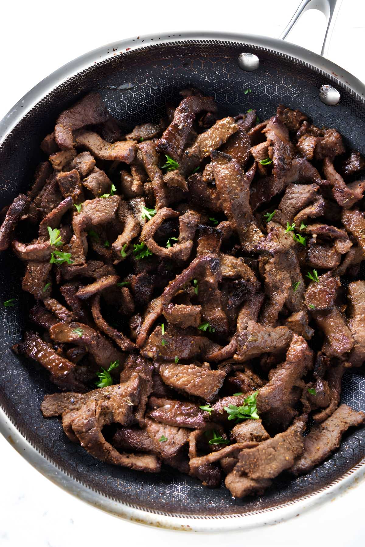 Seasoned beef strips cooking in pan, topped with fresh herb sprigs.