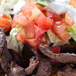 Close-up of beef tostada with lettuce, tomato, avocado, and sour cream.