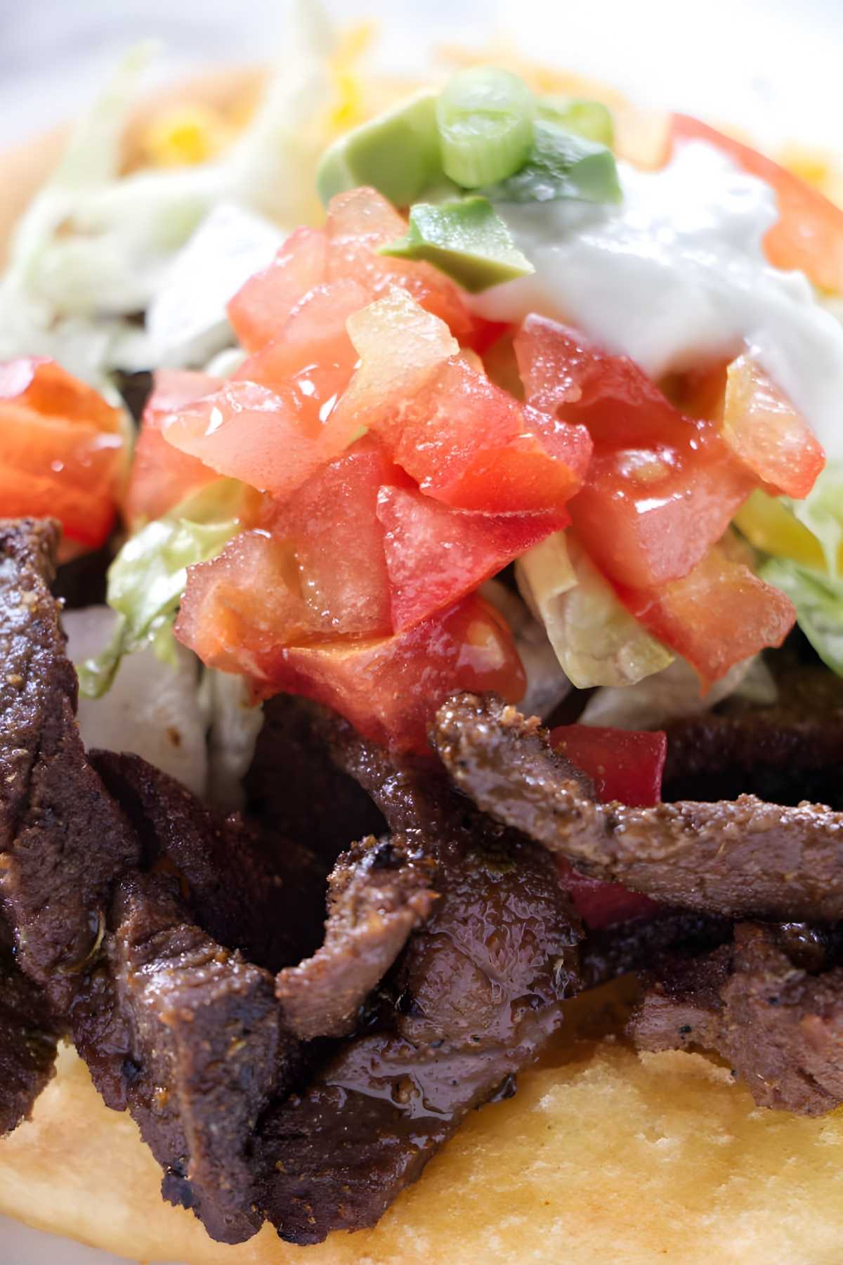 Close-up of beef tostada with lettuce, tomato, avocado, and sour cream.