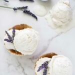 Two waffle bowls with lavender ice cream, lavender garnish, and melting scoop nearby.