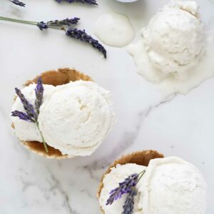 Two waffle bowls with vanilla ice cream, lavender garnish, and melting scoop nearby.