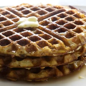 Stack of waffles with melting butter and syrup on a white plate.