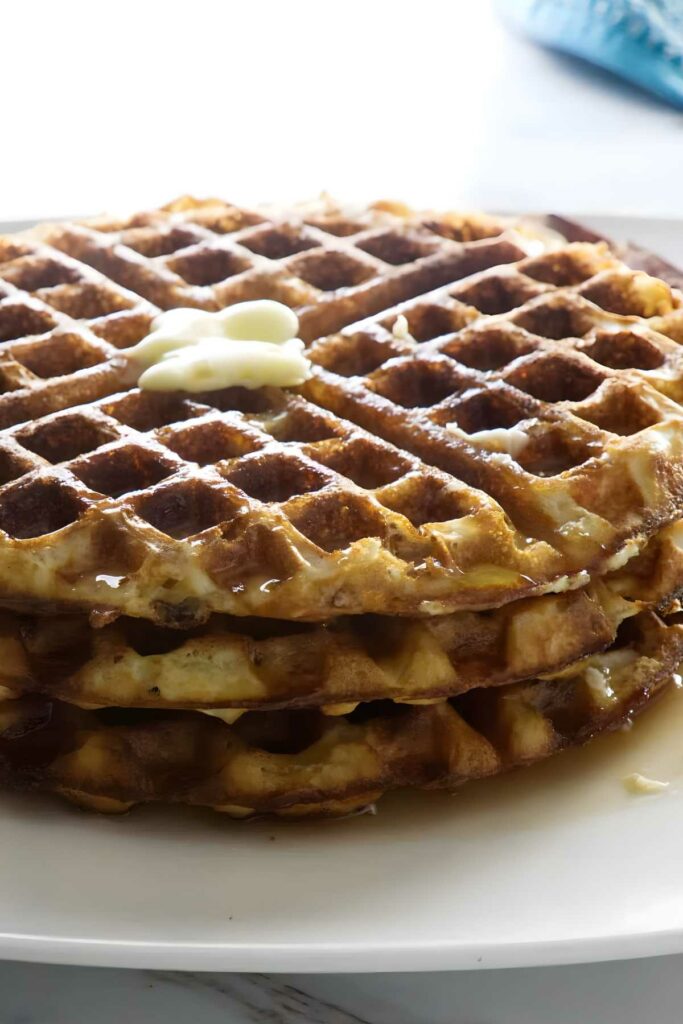 Stack of waffles with melting butter and syrup on a plate.