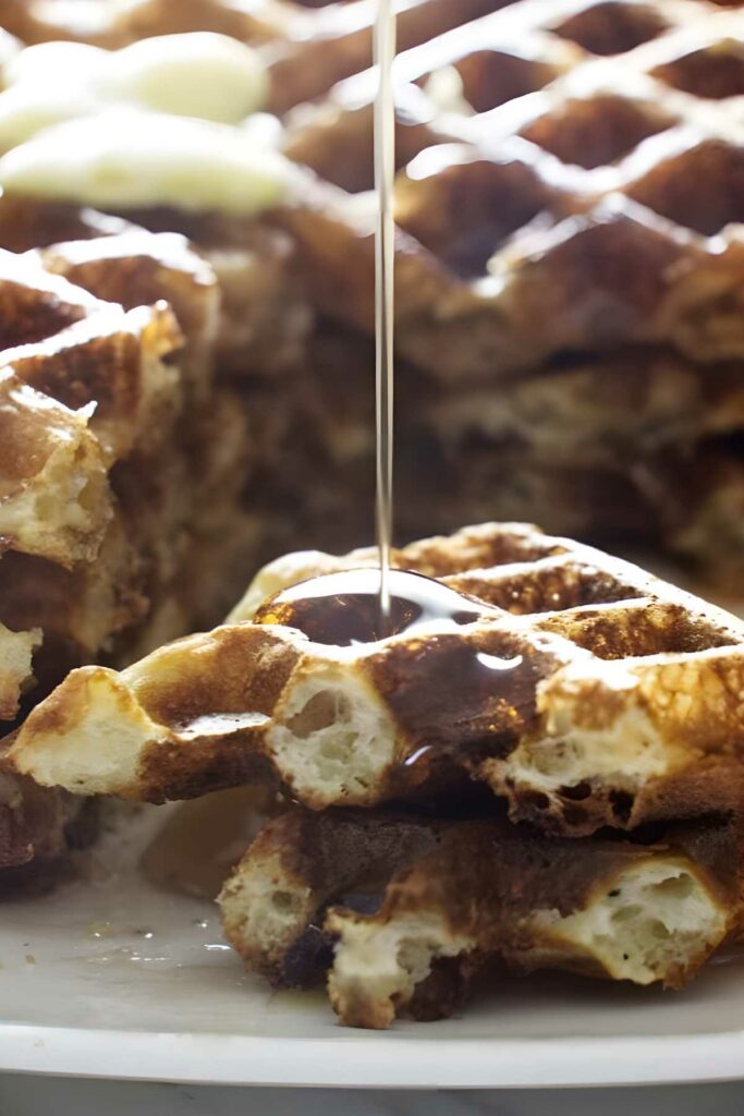 Stacked waffles with syrup pouring and melting butter on top.