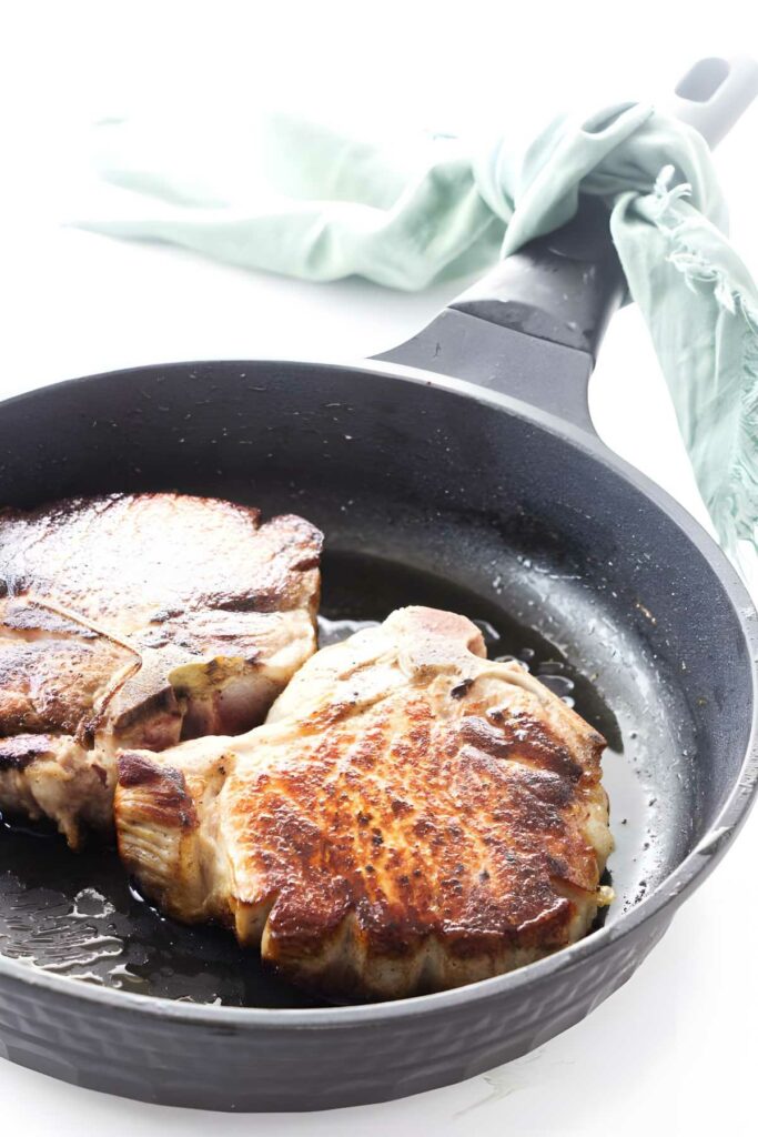 Two browned pork chops in skillet.