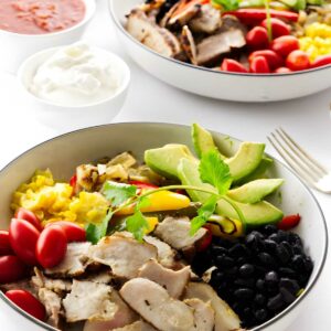 Two bowls of chicken burrito bowls with toppings, salsa, and sour cream.