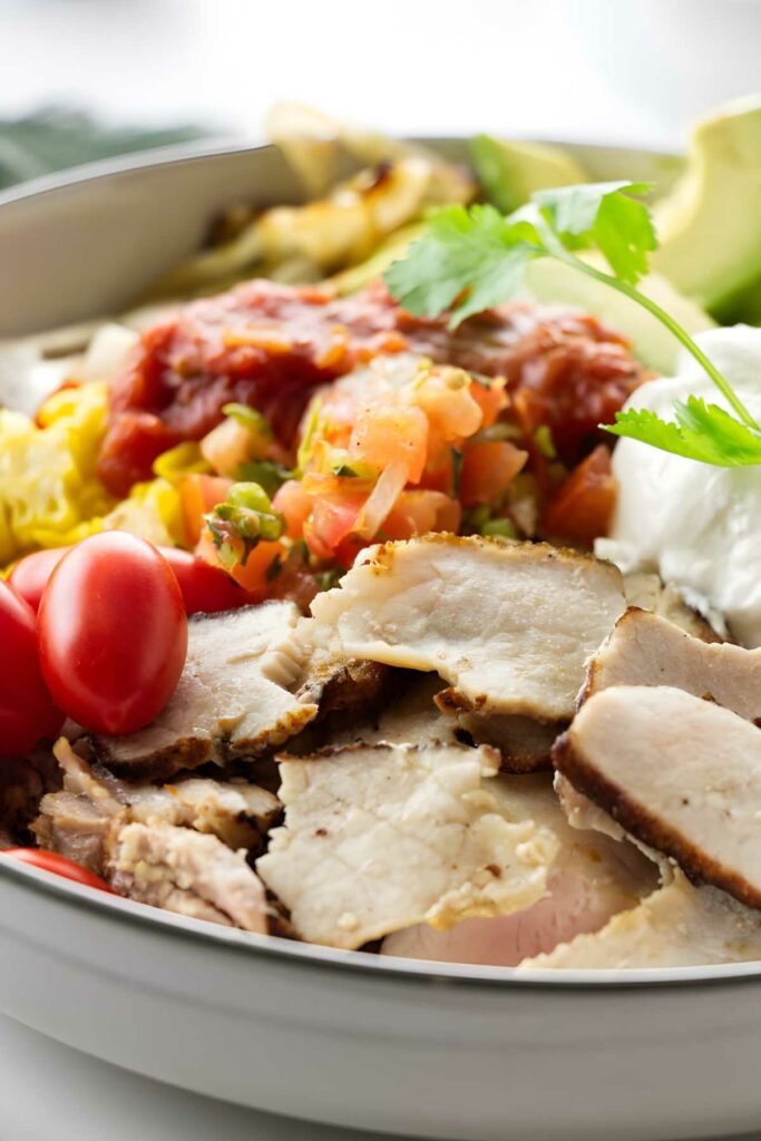 Slices of pork and veggies in a dinner bowl with salsa. 