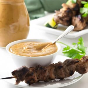 Grilled meat skewers with peanut sauce, fresh herbs, and sauce jar.