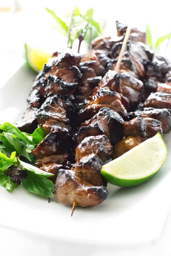 Grilled pork skewers with herbs and lime on a white plate.