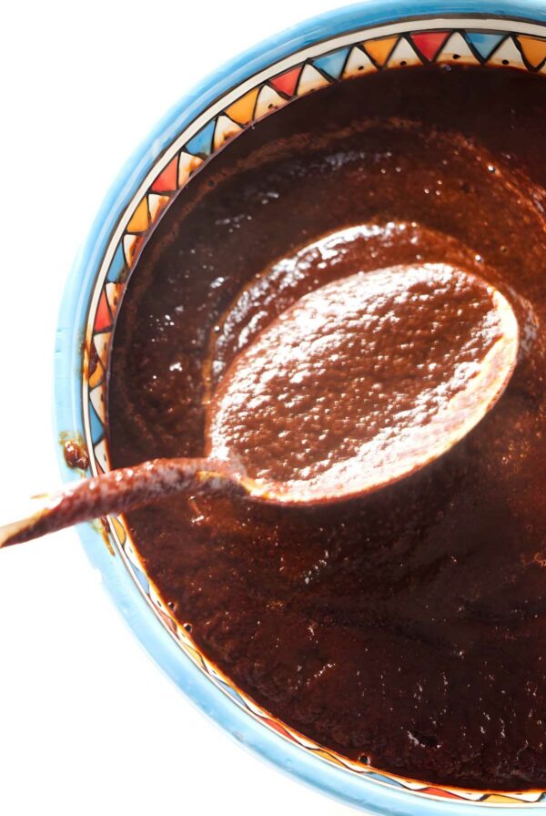 Wooden spoon lifts thick, dark chile sauce from colorful bowl.