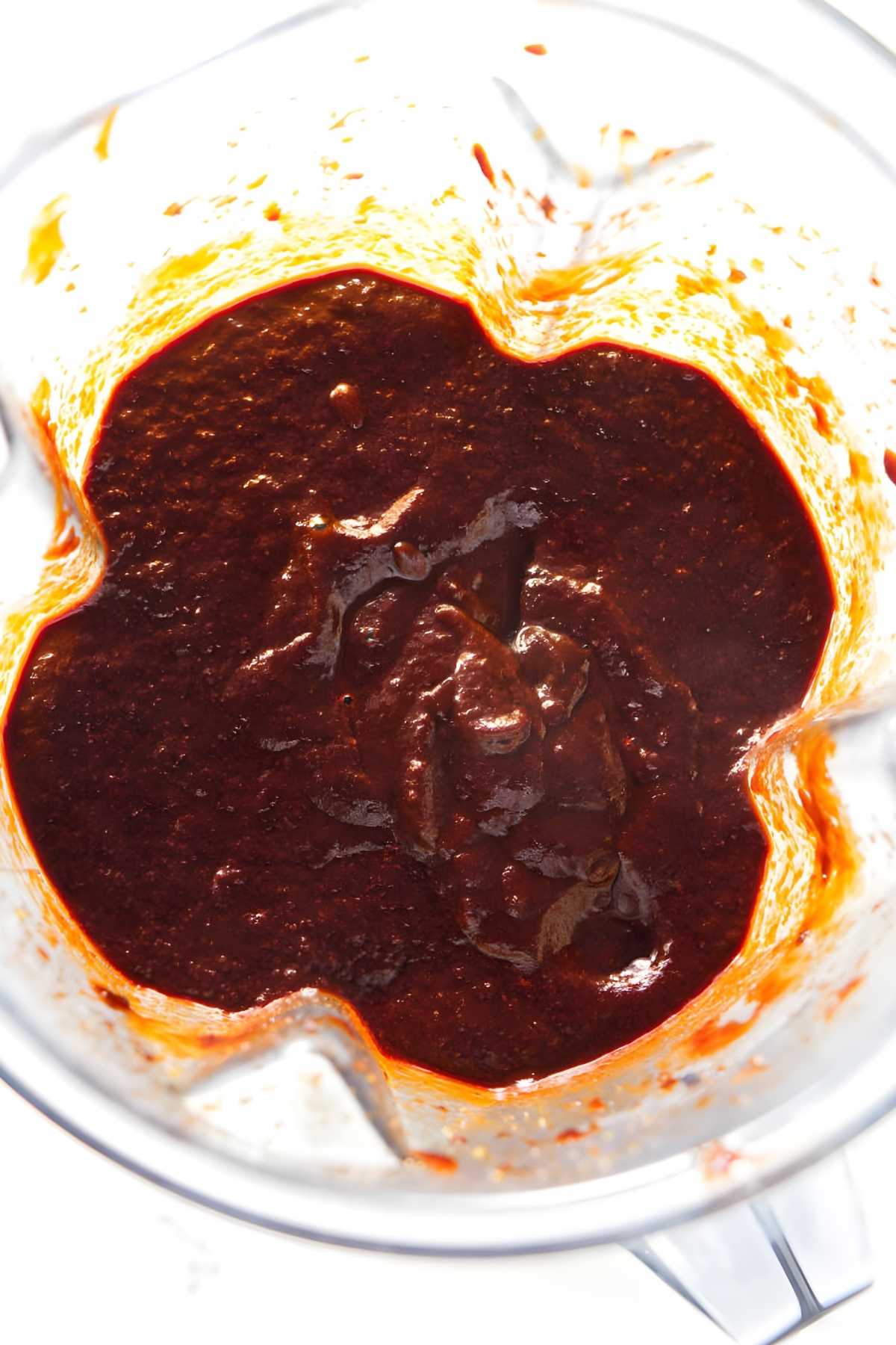 Blender containing thick, dark red chili sauce with splatters on sides.