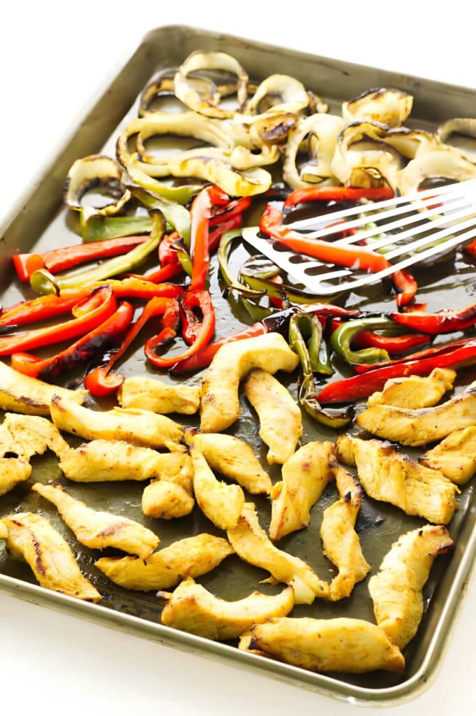 Chicken, bell peppers, and onions on a sheet pan.