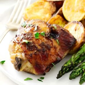 Roasted chicken thigh with herbs, potatoes, asparagus; fork in background.