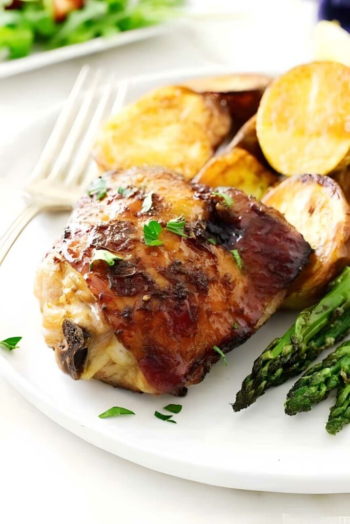 Roasted chicken thigh with herbs, potatoes, asparagus; fork in background.