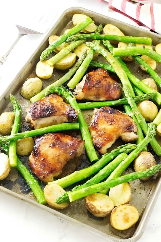 Sheet pan with golden chicken, roasted asparagus, potatoes; red-striped towel nearby.