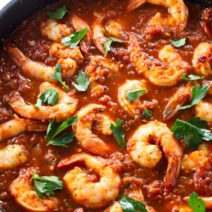 Shrimp cooking in tomato sauce, topped with fresh parsley in skillet.