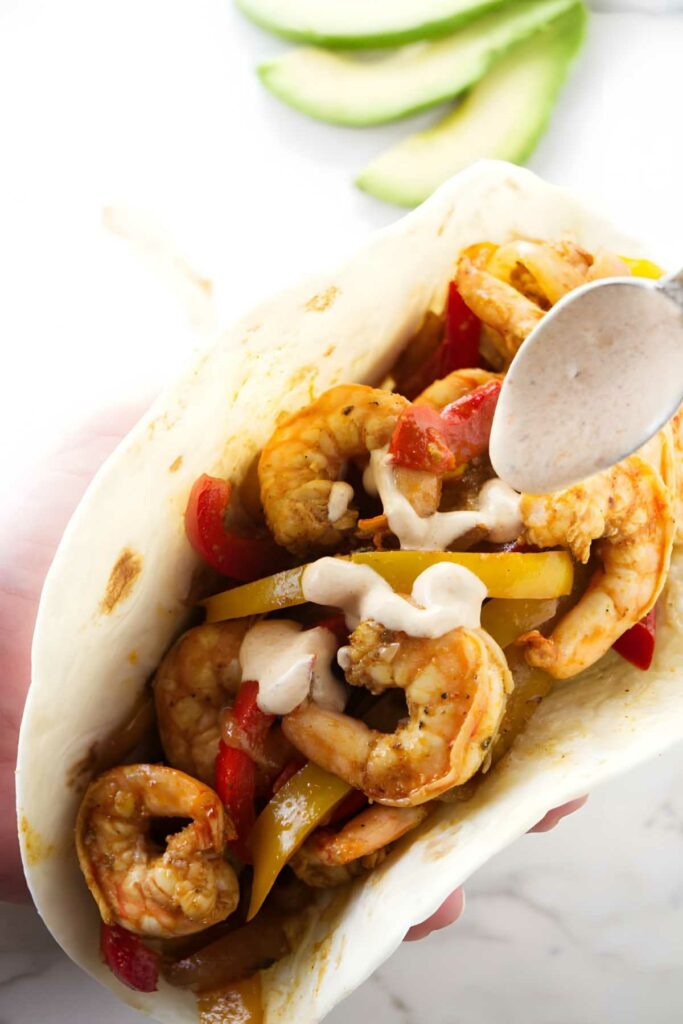 Hand holding a spicy shrimp fajita with charred peppers for and sour cream chipotle sauce.