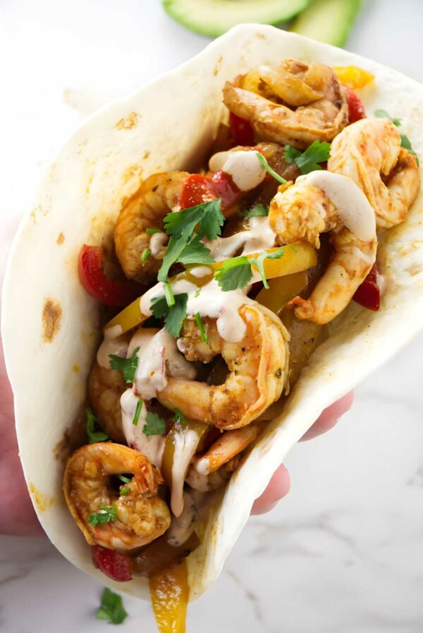 A shrimp fajita with peppers, cilantro, and chipotle cream sauce in a tortilla.