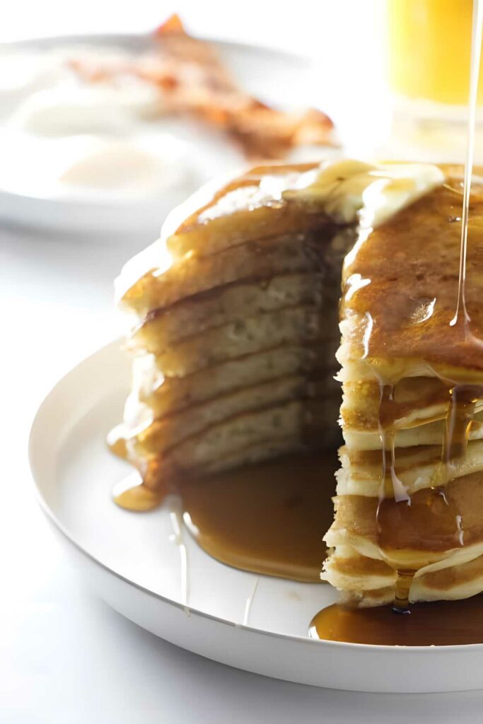 Partially eaten pancake stack with butter and syrup on a plate.