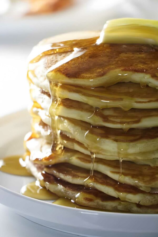 Stack of pancakes with butter and syrup on a white plate.