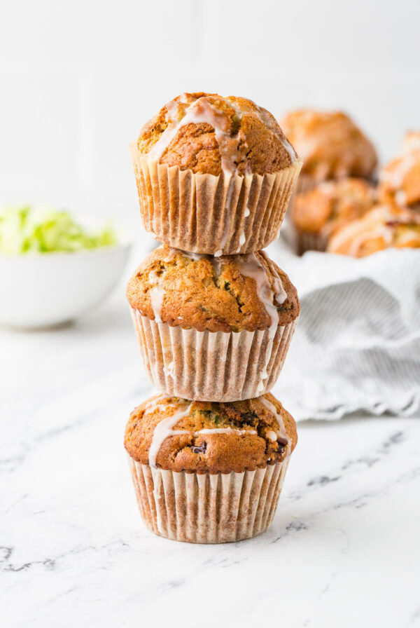 A stack of three sourdough discard zucchini muffins on a white counter.