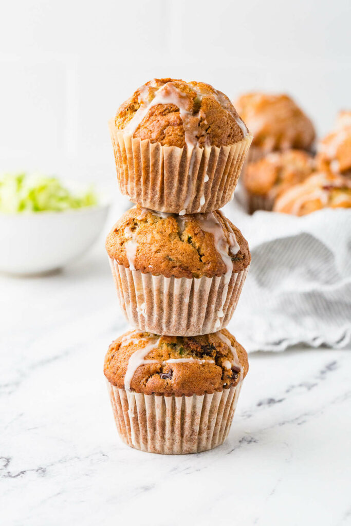 A stack of three sourdough discard zucchini muffins on a white counter.