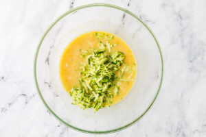 Adding grated zucchini to a mixing bowl with muffin batter.