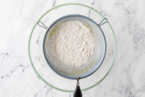 Sifting flour into a mixing bowl with zucchini and sourdough discard.
