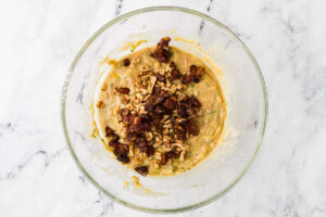 Adding walnuts and chopped dates to muffin batter in a mixing bowl.