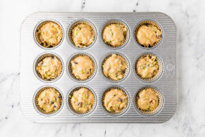 Adding batter to muffin tins for date and nut zucchini muffins with discard.