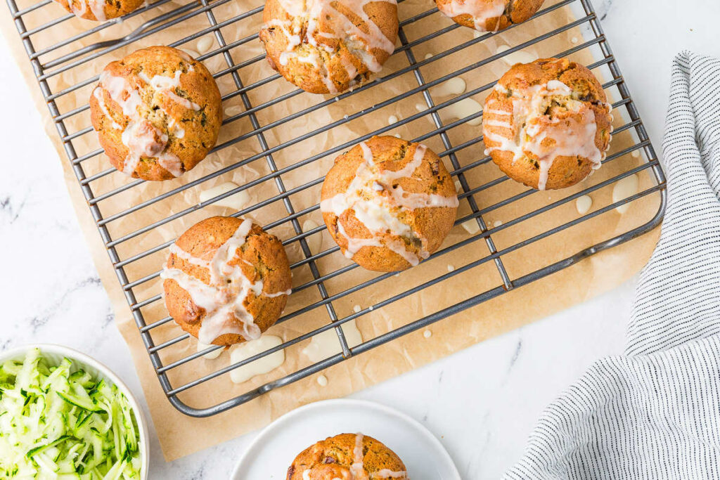 Drizzling glaze on top of muffins on a cooling rack.