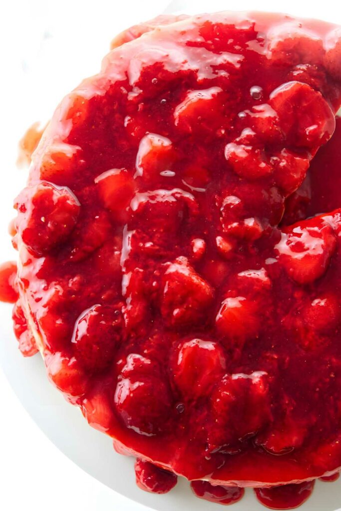 Close-up of cheesecake with strawberry sauce and whole strawberries.