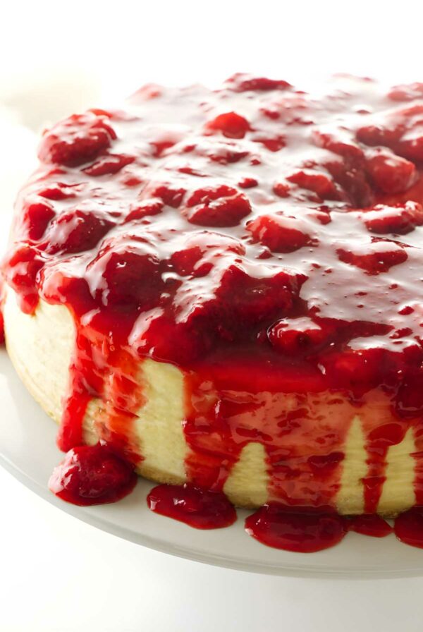 Cheesecake with strawberry sauce dripping down, on white plate, light background.
