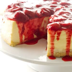 A sliced cheesecake with strawberry topping on a cake plate.