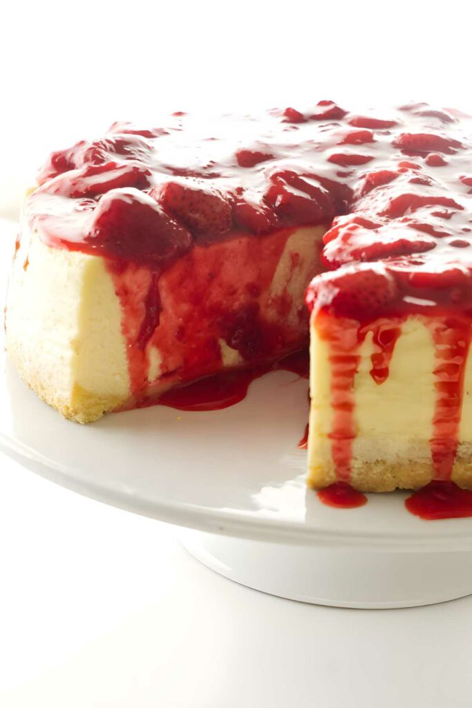 A sliced cheesecake with strawberry topping on a cake plate.