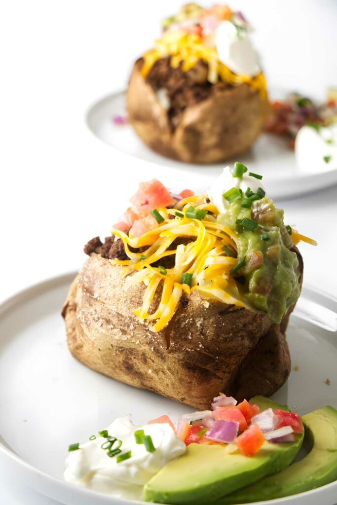Two baked potatoes topped with taco fixings