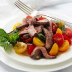 A tomato and herb steak salad on a white plate.