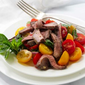 A tomato and herb steak salad on a white plate.