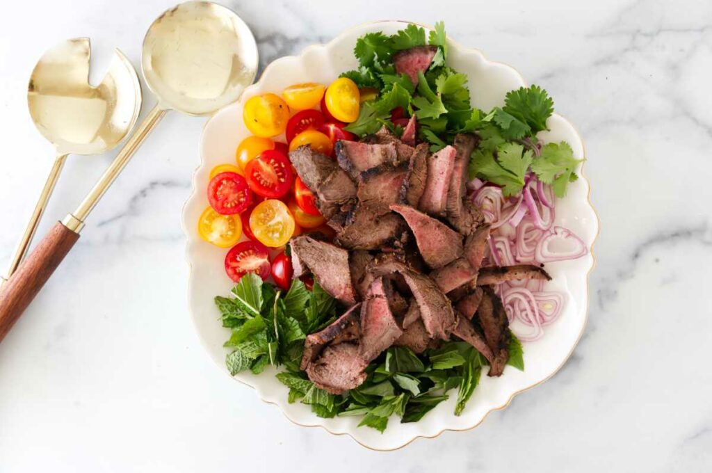 A salad plate with steak strips, fresh herbs, shallots, and tomatoes.