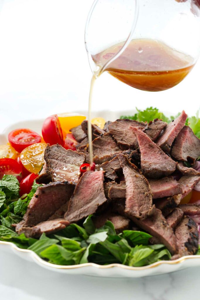 Pouring a chili lime dressing over a steak salad.